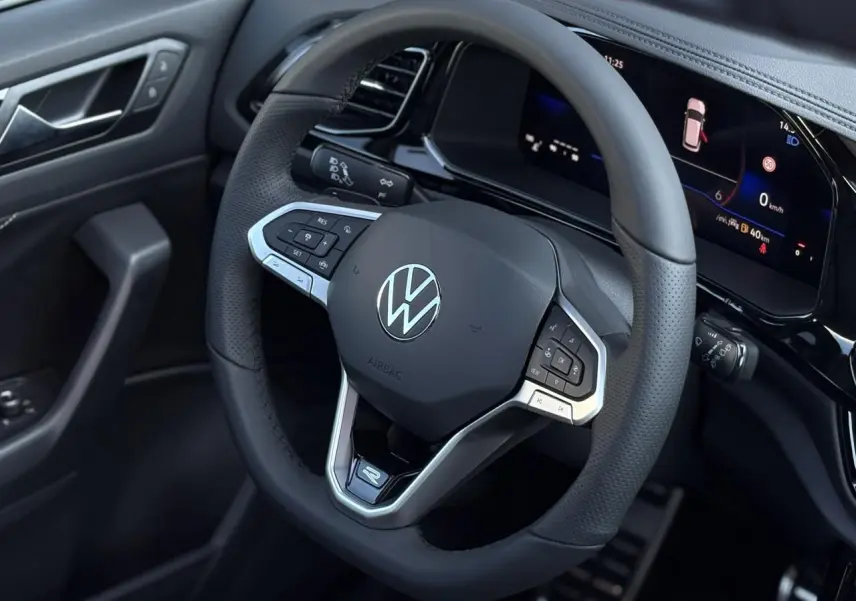 Gros plan sur le volant cuir noir avec logo VW et combiné digital du tableau de bord du Volkswagen T-Roc R-Line.