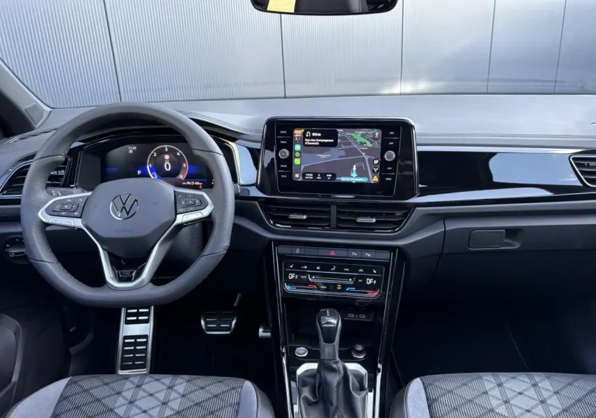 Vue frontale de l'habitacle du Volkswagen T-Roc 2025, tableau de bord noir avec écran tactile et volant multifonction.