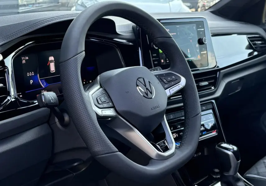 Vue intérieure centrée sur le volant sport multifonction noir du Volkswagen T-Roc 2025 avec tableau de bord digital et écran tactile.