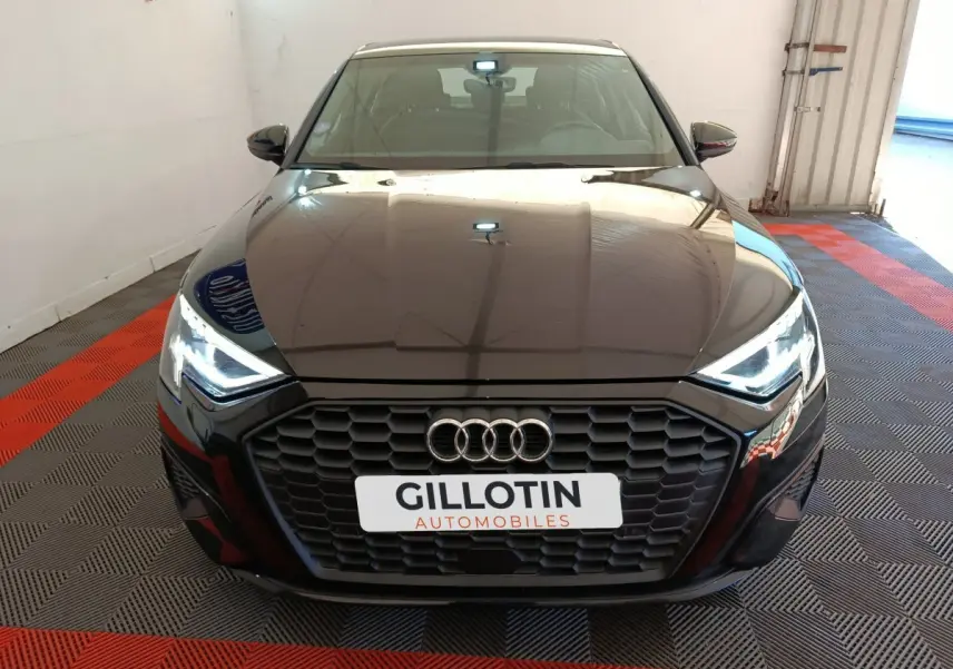 Vue frontale d'une Audi A3 noire 2022 avec calandre hexagonale et phares LED allumés dans un showroom.