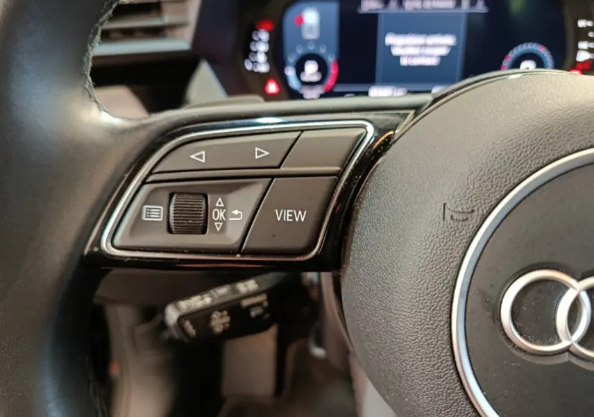 Gros plan sur le volant cuir noir de l'Audi A3 2022 avec commandes multifonctions et combiné d'instruments numérique.