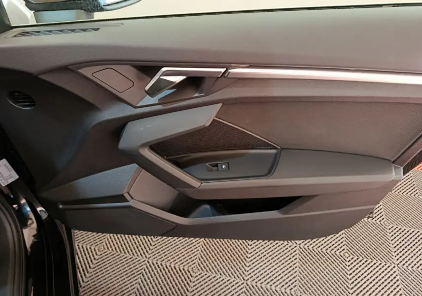 Vue rapprochée de la porte avant gauche noire de l'Audi A3 30 TFSI MHEV avec poignée et commande de fenêtre intégrées.