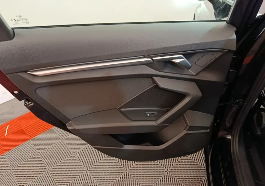 Porte intérieure côté gauche noire de l'Audi A3 30 TFSI MHEV 2022 avec poignée argentée et commande de vitre.