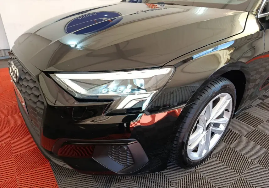 Vue 3/4 avant droit d'une Audi A3 noire mettant en valeur son phare LED et sa calandre distinctive.