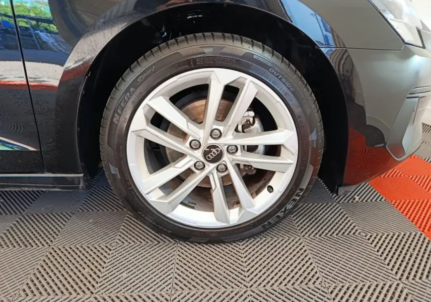 Gros plan sur la roue avant gauche noire d'une Audi A3 30 TFSI MHEV avec jante argentée à 5 branches doubles.