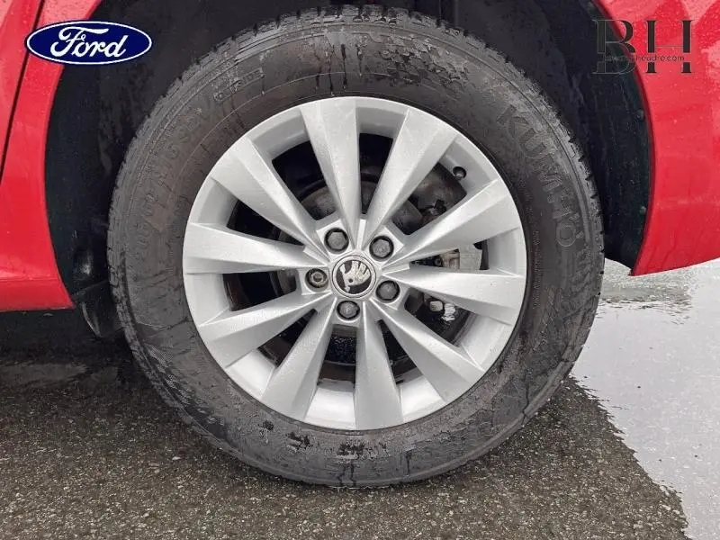 Gros plan sur la roue avant gauche d’un Skoda Kamiq rouge Velvet avec jante alu argentée et logo Skoda au centre.