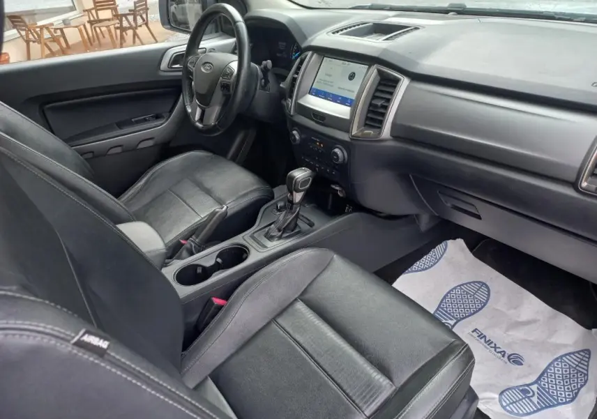 Vue intérieure côté conducteur du Ford Ranger blanc 2022, mettant en valeur les sièges cuir noirs et la console centrale avec boîte automatique.