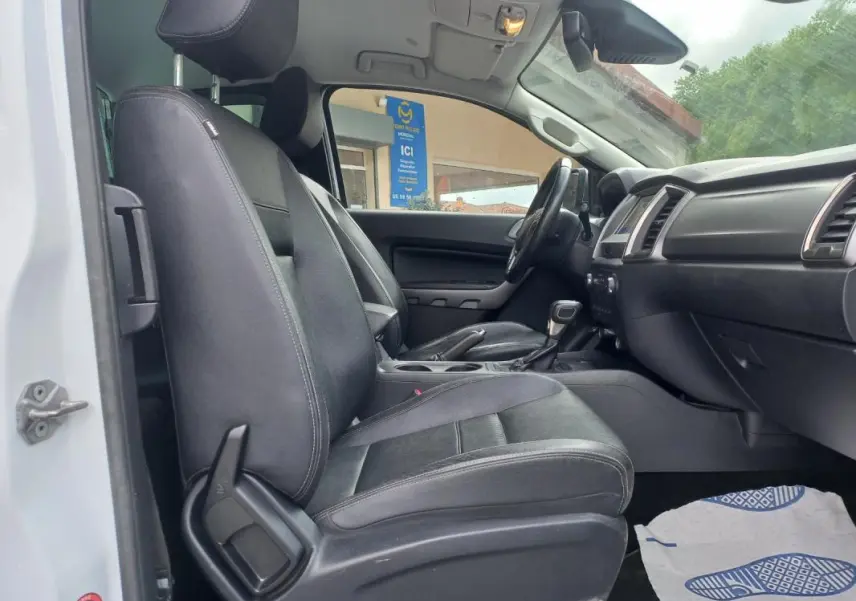 Vue intérieure côté conducteur du Ford Ranger Super Cabine Limited 2022 blanc, sièges noirs en tissu et tableau de bord visible.