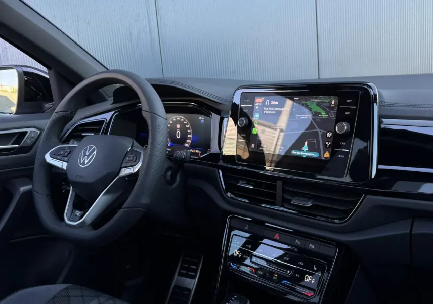 Intérieur du Volkswagen T-Roc 2025 vu côté conducteur, volant cuir R-Line et écran tactile avec navigation affichée.
