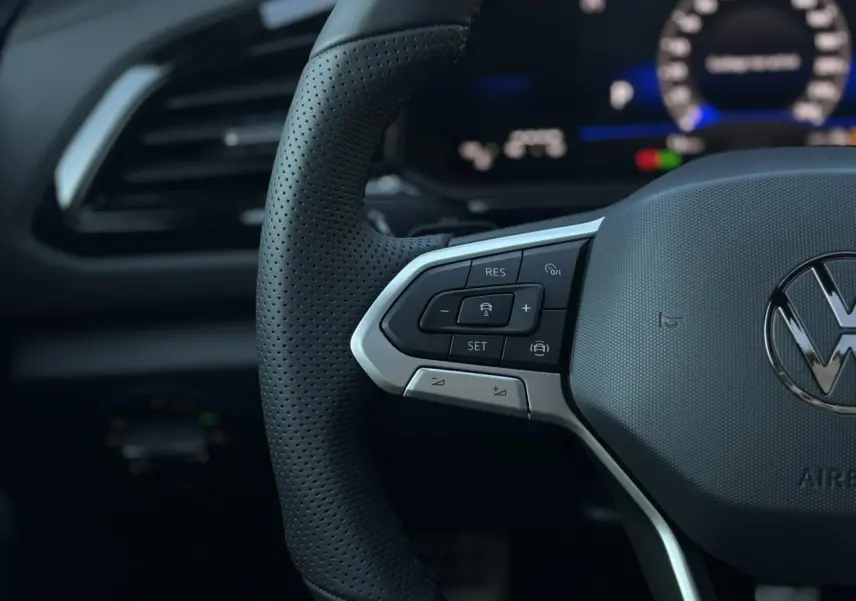 Gros plan sur le volant cuir perforé du Volkswagen T-Roc 2025 avec commandes multifonctions et logo VW central.