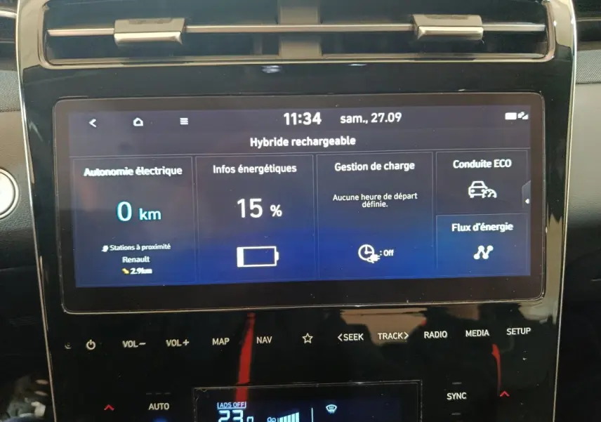 Écran tactile central du Hyundai Tucson marron affichant l'autonomie électrique et gestion de charge en vue frontale rapprochée.