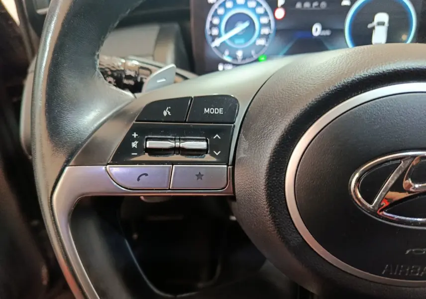 Gros plan sur le côté gauche du volant noir du Hyundai Tucson 2022, avec commandes audio et affichage digital en arrière-plan.