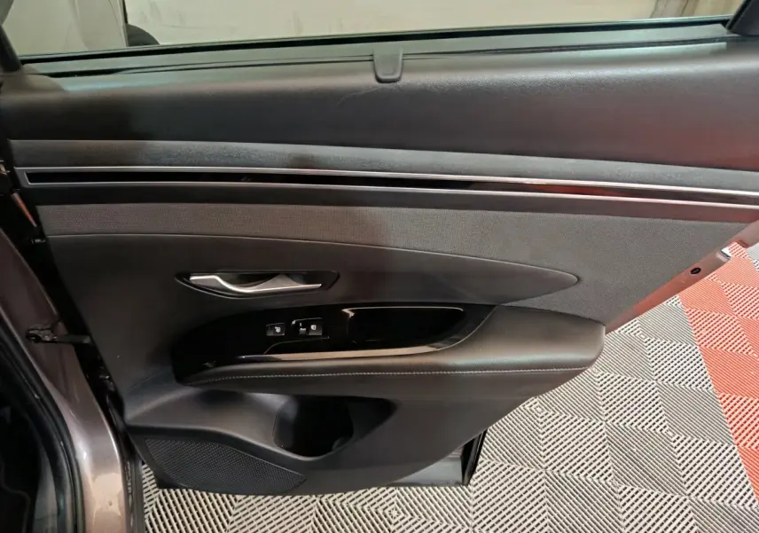 Vue intérieure côté gauche de la porte avant du Hyundai Tucson marron, avec commandes de vitres et poignée argentée.