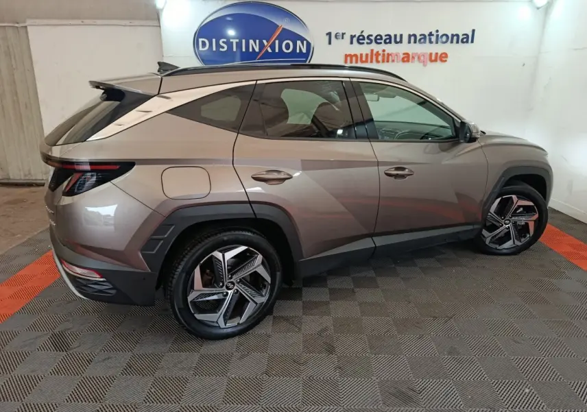 Vue côté gauche d'un Hyundai Tucson marron 2022 hybride rechargeable, avec jantes alliage et toit ouvrant en intérieur showroom.