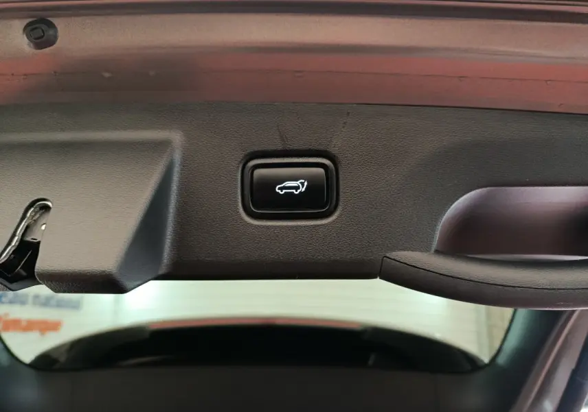 Bouton d'ouverture électrique du coffre sur la trappe intérieure d'un Hyundai Tucson marron 2022 hybride rechargeable.