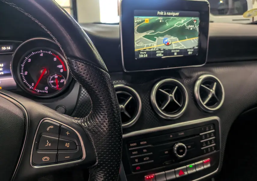 Vue intérieure rapprochée du tableau de bord et volant en cuir noir d'une Mercedes Classe A 200d avec écran de navigation allumé.