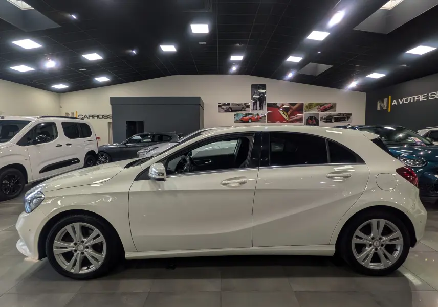Profil côté gauche d'une Mercedes Classe A 200d blanche de 2016, avec jantes alliage et vitres teintées, en intérieur showroom.