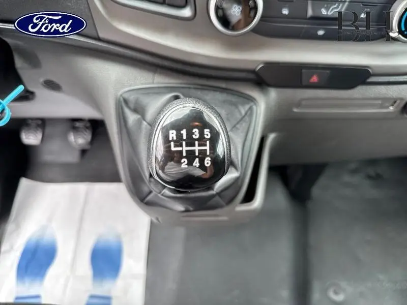 Gros plan sur le levier de vitesses manuel noir du Ford Transit Custom blanc, avec tableau de bord gris en arrière-plan.