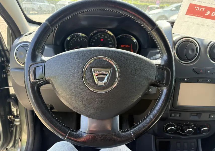 Vue intérieure centrée sur le volant noir du Dacia Duster 1.5 DCI 110 2014, avec tableau de bord et console centrale visibles.