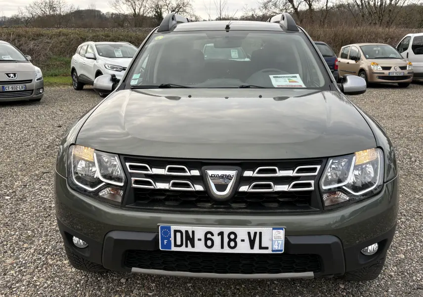 Vue de face d’un Dacia Duster 1.5 DCI 110 vert foncé avec calandre chromée et phares allumés sur un parking.