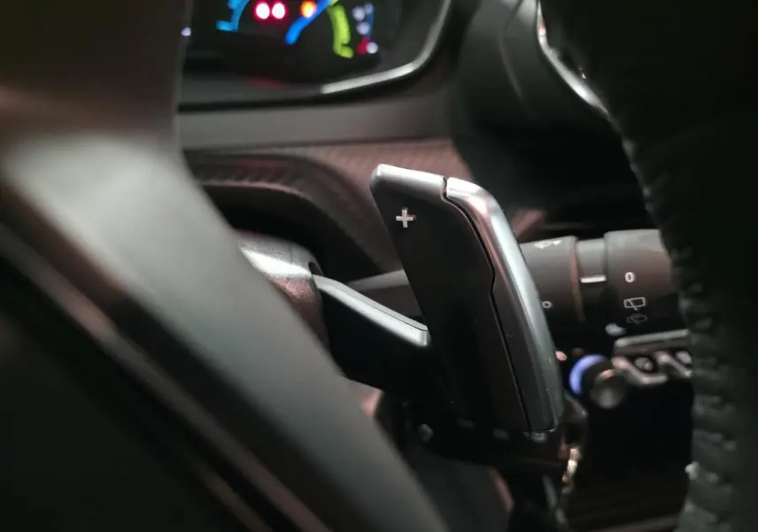 Gros plan sur la palette de changement de vitesse + au volant cuir noir du Peugeot 2008 gris hybride 2025.