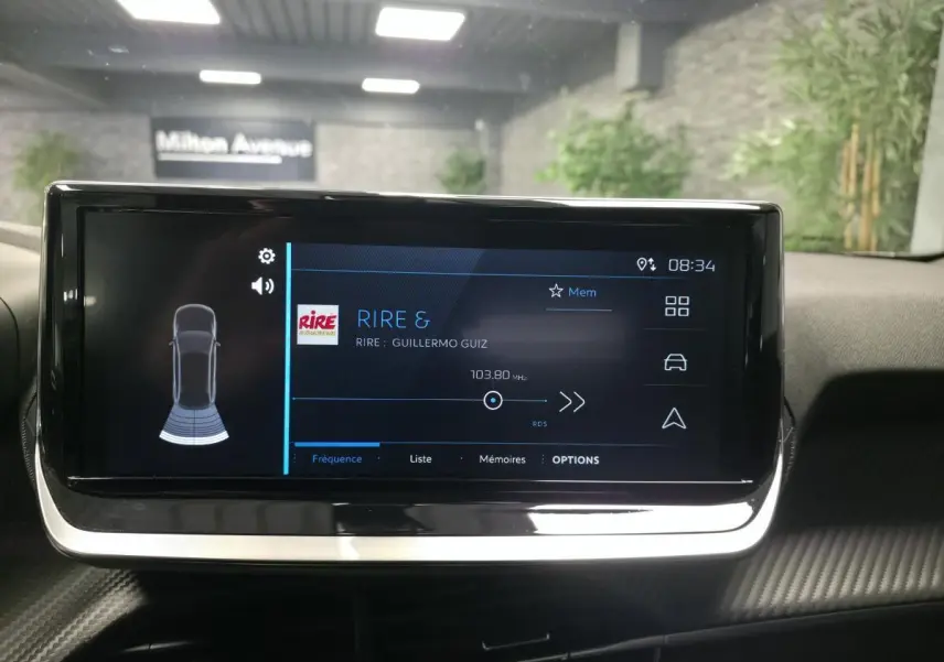 Écran tactile central du Peugeot 2008 gris, affichant la radio et l'aide au stationnement arrière.
