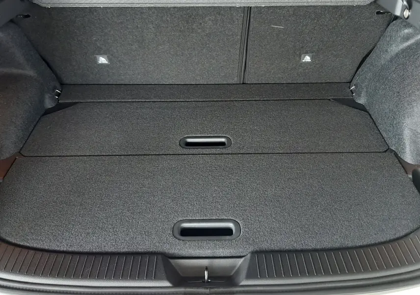 Coffre ouvert du Nissan Qashqai blanc lunaire 2022, montrant un espace de rangement plat et compartimenté en tissu gris foncé.