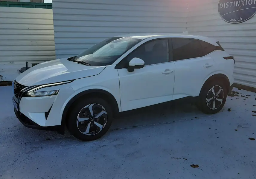 Nissan Qashqai blanc lunaire vu de profil côté gauche, avec jantes alliage et vitres teintées, stationné en extérieur.