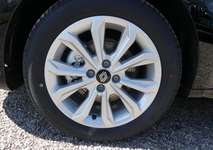 Gros plan sur la roue avant droite d'une Renault Clio noire métallisée avec jante argentée à motifs géométriques.