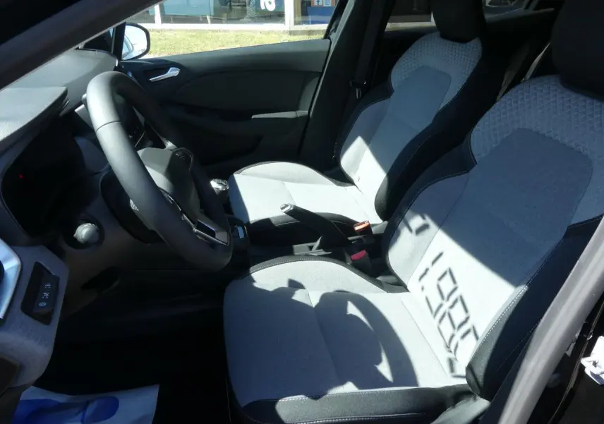 Intérieur avant droit de la Renault Clio 2025, sièges tissu gris avec motifs 3D et volant multifonction noir.