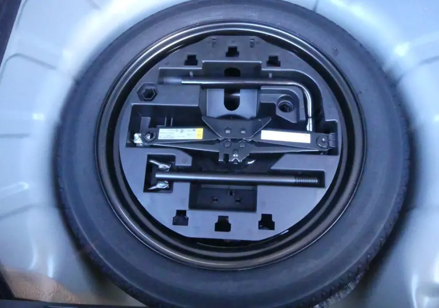 Roue de secours temporaire avec outillage intégré dans le coffre d'une Renault Clio noire métallisée 2025.