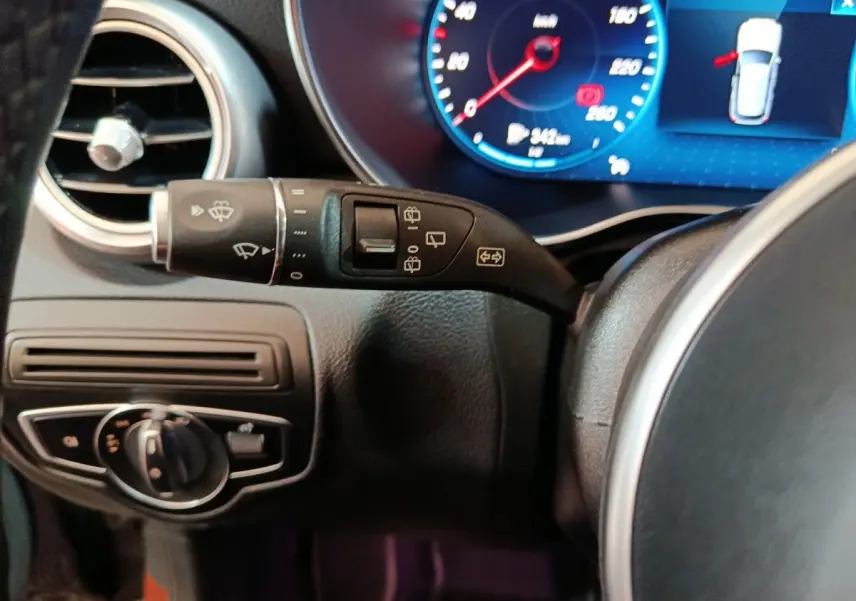 Gros plan sur la commande d’essuie-glace et tableau de bord numérique bleu d’une Mercedes GLC 300 e Business Line noire.