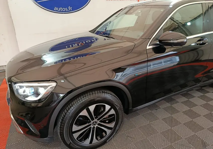 Vue 3/4 avant droit d'un Mercedes GLC 300 e Business Line noir brillant avec jantes alliage et badge hybride sur aile avant.