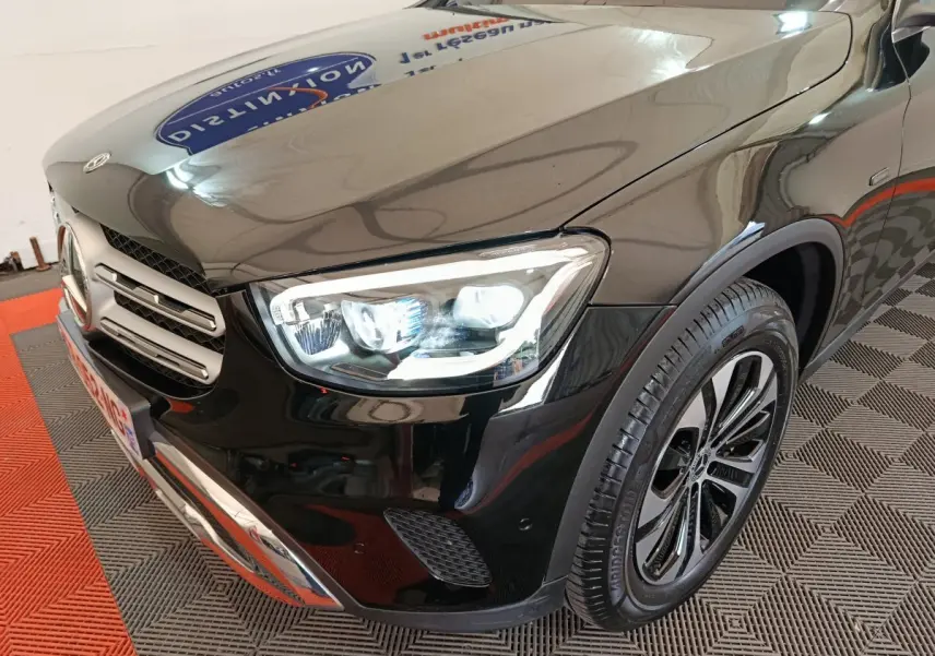 Vue 3/4 avant droit d'un Mercedes GLC 300 e Business Line noir avec phares LED allumés et jantes alliage distinctives.