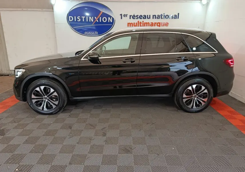 Profil côté gauche d'un Mercedes GLC 300 e Business Line noir, hybride rechargeable, sur sol damier en intérieur showroom.