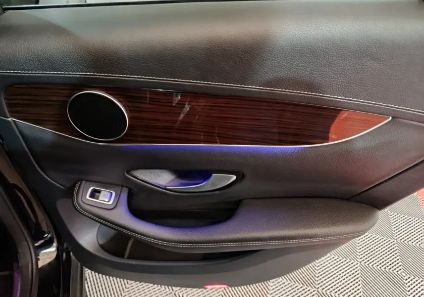 Vue intérieure côté gauche de la porte noire du Mercedes GLC 300 e Business Line avec garniture bois et éclairage d'ambiance bleu