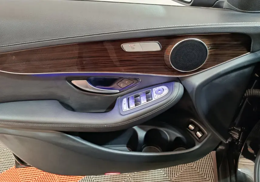 Gros plan sur la porte avant gauche noire du Mercedes GLC 300 e Business Line avec garniture bois et commandes électriques.