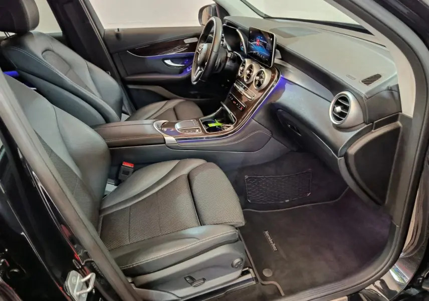 Intérieur avant droit d’un Mercedes GLC 300 e Business Line 2020 noir, avec tableau de bord moderne et éclairage d’ambiance bleu.