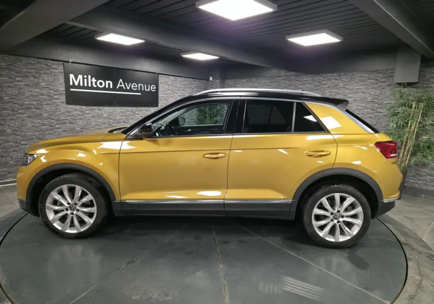 Volkswagen T-Roc jaune Curcuma vu de profil côté gauche avec toit noir et jantes alliage 18 pouces.