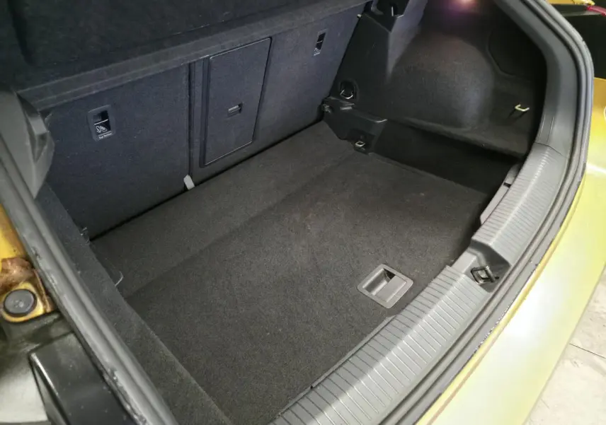 Coffre ouvert vu de dessus du Volkswagen T-Roc orange, montrant l'espace de rangement vide et la moquette noire.