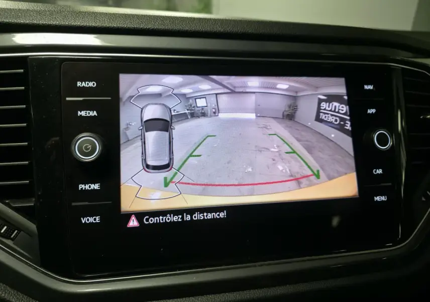 Écran tactile de la Volkswagen T-Roc affichant la caméra de recul avec alertes de distance en intérieur de garage.