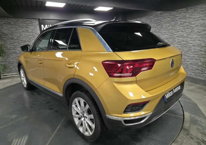 Vue 3/4 arrière droite d'un Volkswagen T-Roc jaune Curcuma avec toit noir et jantes alliage 18 pouces.