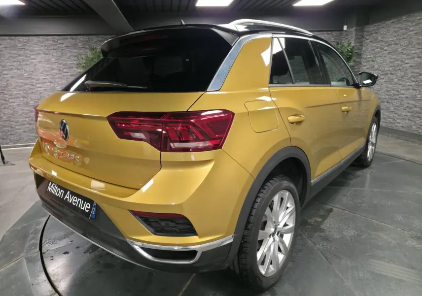 Vue 3/4 arrière droite d'un Volkswagen T-Roc jaune Curcuma avec toit noir et jantes alliage 18 pouces.