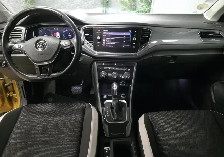 Vue intérieure avant du Volkswagen T-Roc 2021, tableau de bord noir avec écran tactile et volant multifonction cuir.