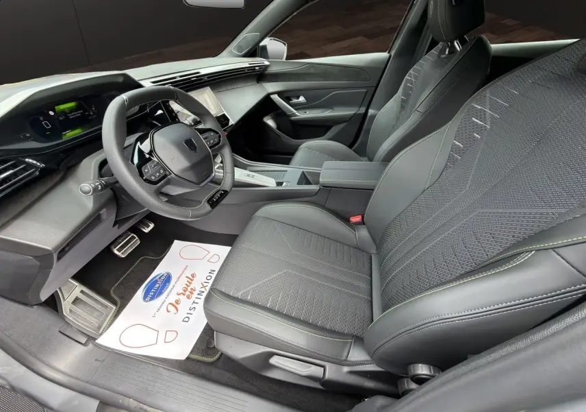 Vue intérieure côté conducteur de la Peugeot 308 GT 2026, sièges noirs avec surpiqûres vertes et tableau de bord numérique.