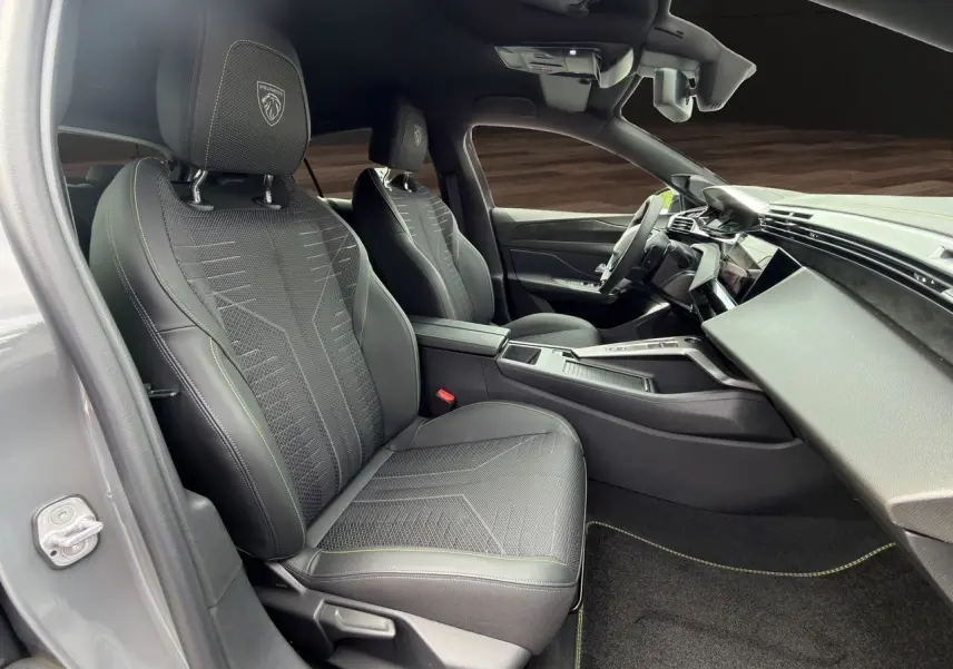 Vue intérieure côté conducteur de la Peugeot 308 GT 2026 gris selenium, sièges noirs avec surpiqûres vertes et tableau de bord moderne.