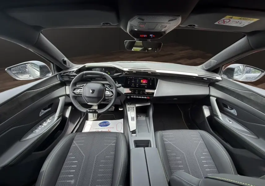 Vue intérieure avant de la Peugeot 308 GT 2026, tableau de bord moderne avec volant compact et sièges tissu noir.