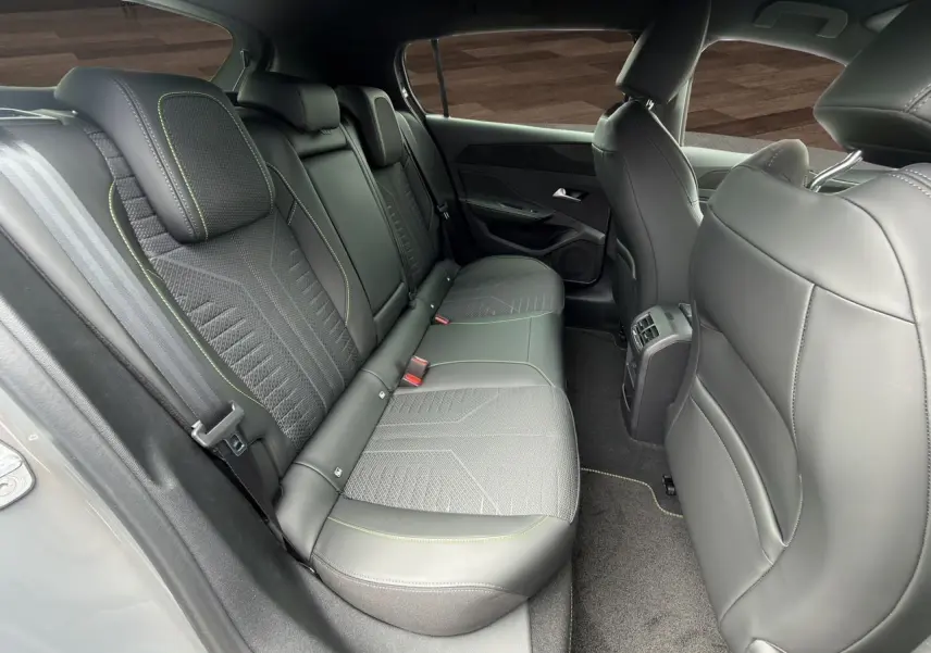 Vue intérieure arrière côté droit de la Peugeot 308 GT 2026, sièges noirs avec surpiqûres vert Adamite et tissu Uzila embossé.