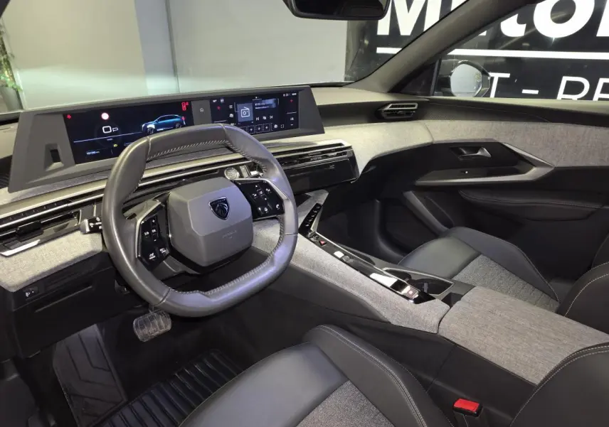 Intérieur avant droit du Peugeot 3008 Hybrid 2025, tableau de bord et volant cuir avec écrans numériques panoramiques.