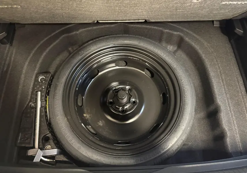 Roue de secours noire en acier dans le coffre d'une Volkswagen Golf 1.5 eTSI 116 DSG7 Bleu Anémone, vue de dessus.